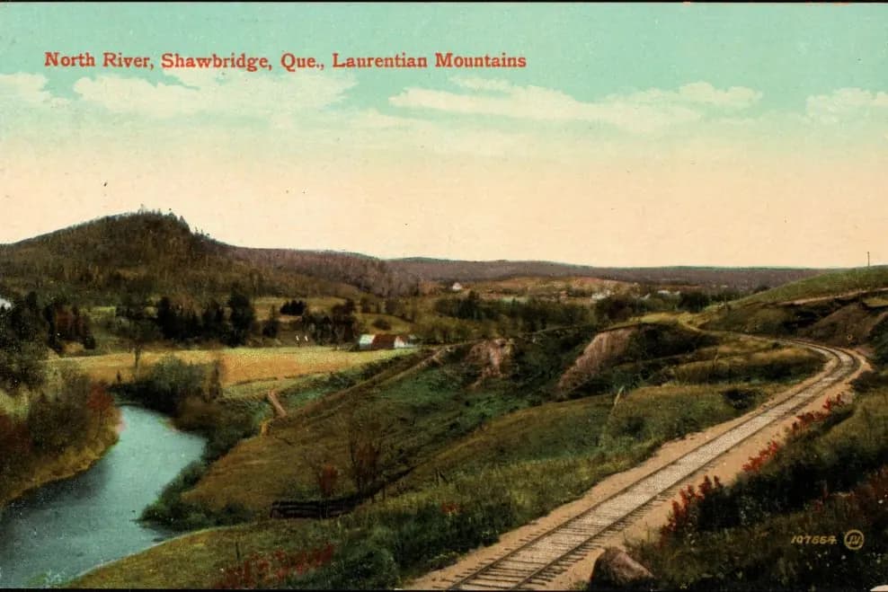 Carte postale ancienne en couleurs : la rivière du Nord serpente près de la voie ferrée, à Shawbridge, les collines derrière.