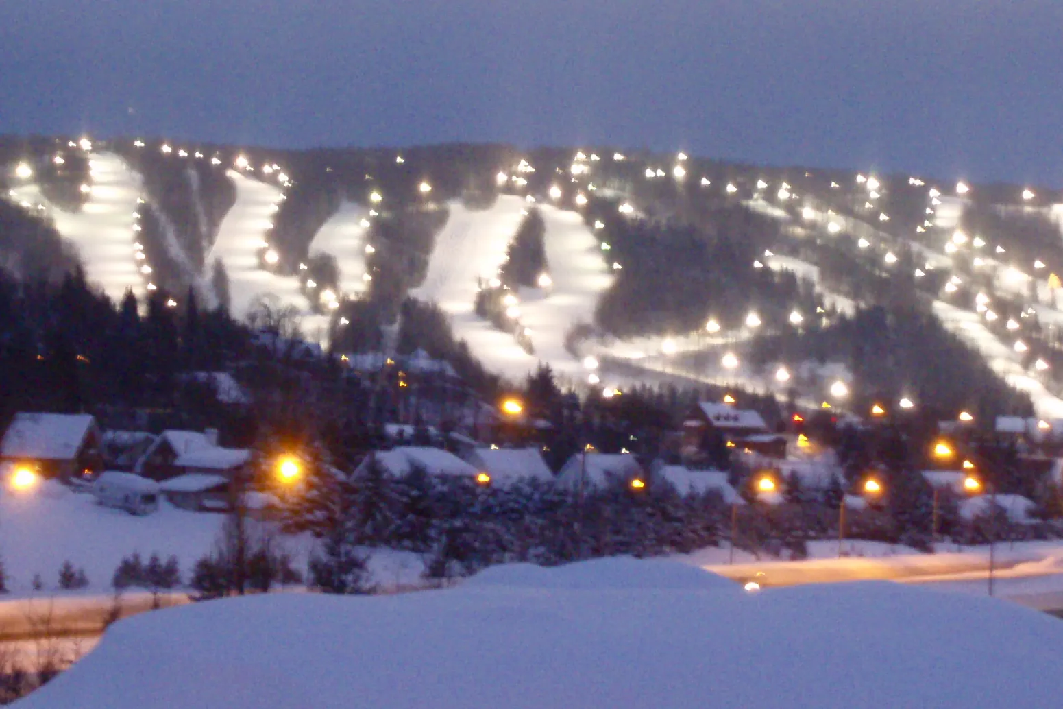 Les pistes de ski éclairées du mont Saint-Sauveur, la nuit, au-dessus des maisons enneigées du village.