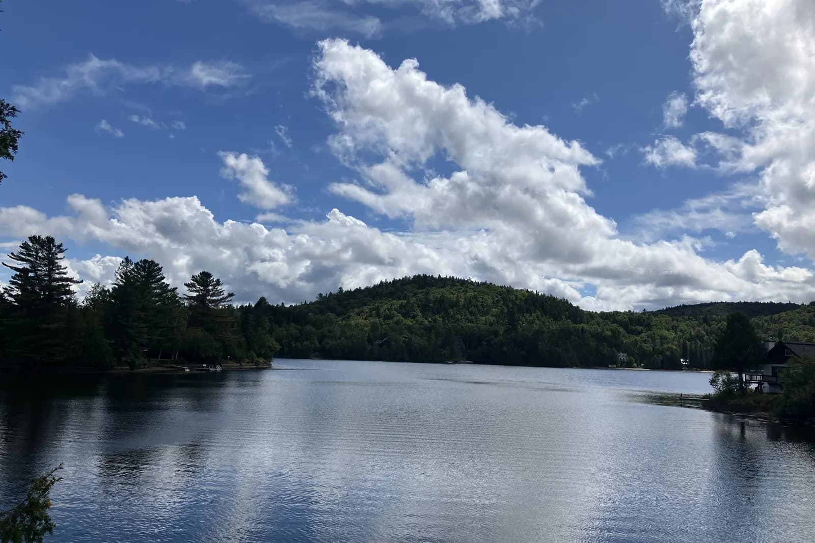 Le lac Raymond, calme, bordé de forêt, sous un ciel de cumulus.