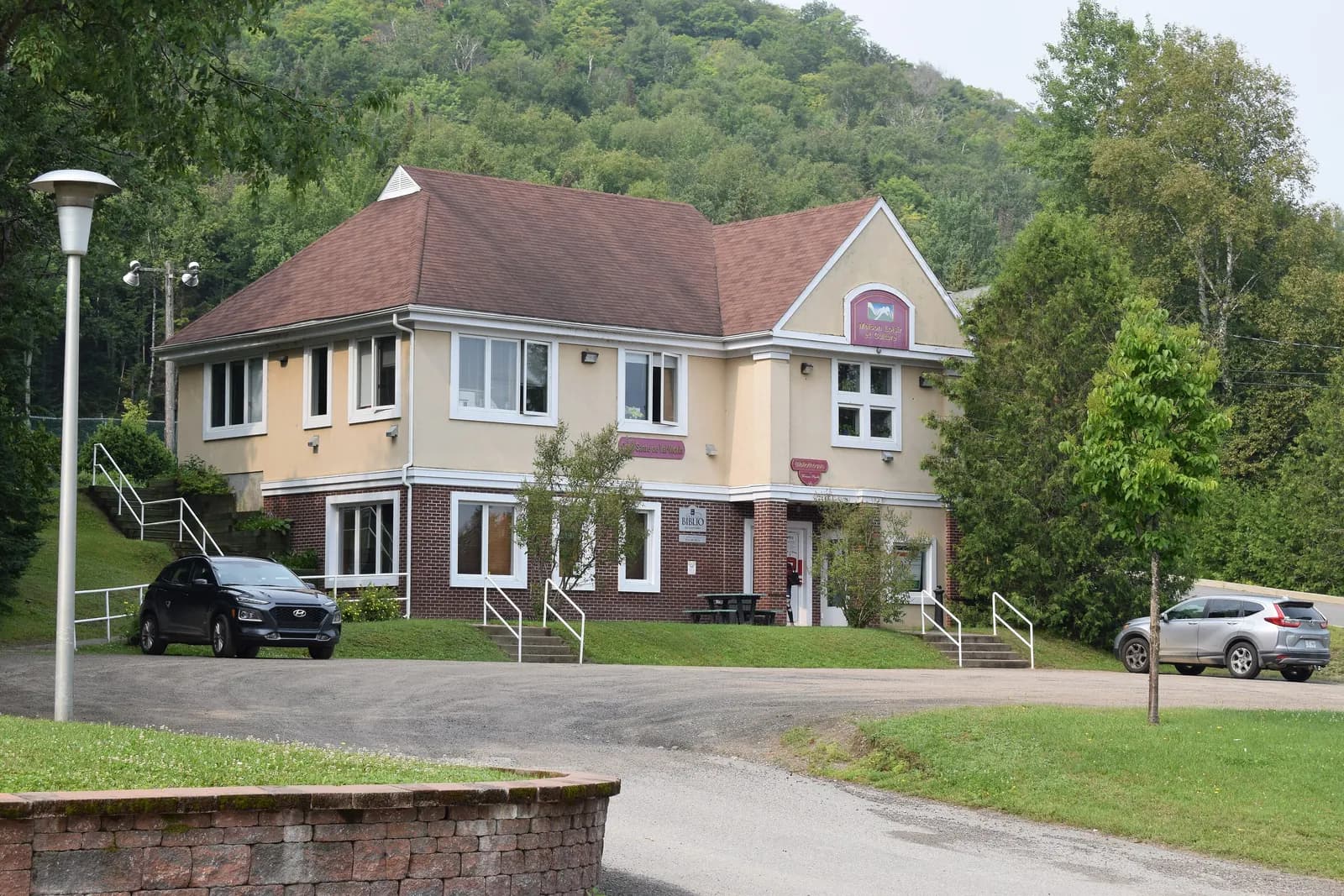 La Maison loisir et culture de Val-Morin, un bâtiment beige à toit brun au pied d’une colline boisée.